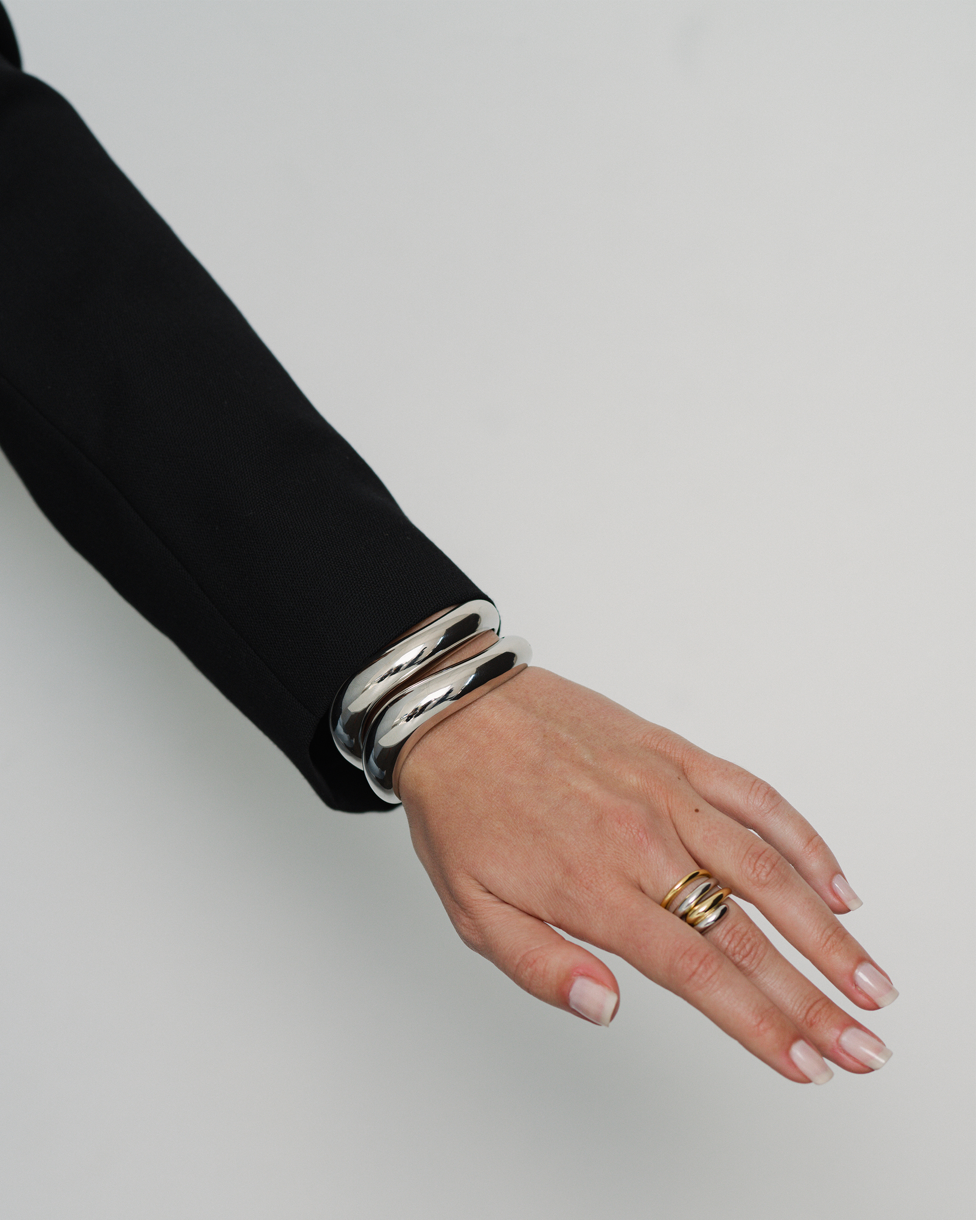 Hand wearing a silver bracelet and gold ring on a plain background