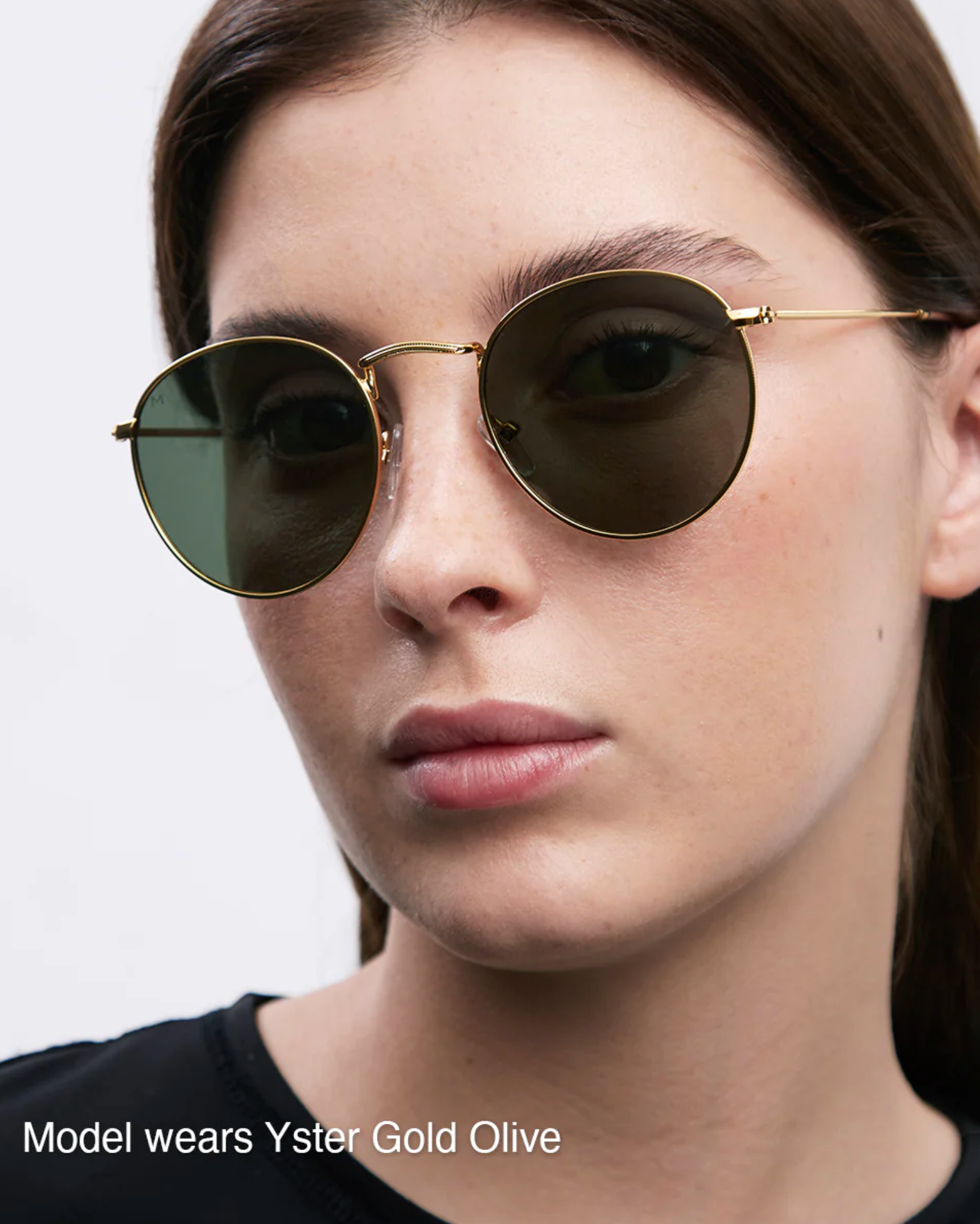 Woman wearing Yster Gold Olive sunglasses with a plain background