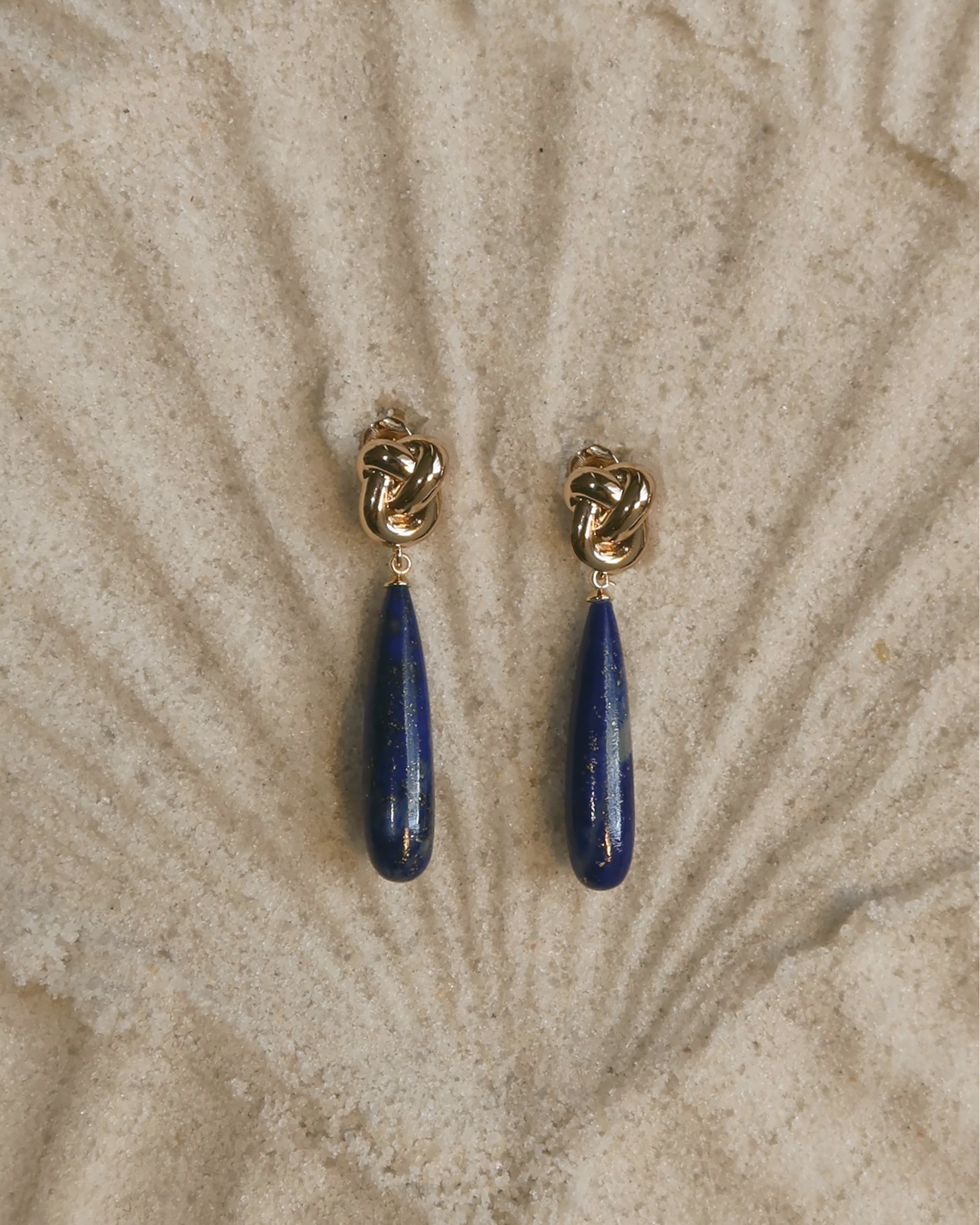 Pair of earrings with blue teardrop-shaped stones on a textured beige background