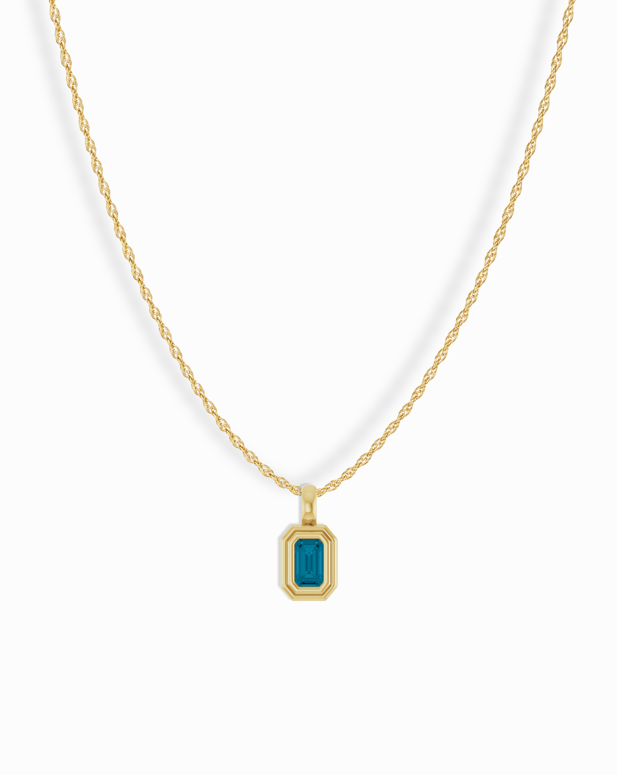 A Mod + Jo 14k Birthstone Pendant Necklace featuring a gold chain and an emerald-cut blue gemstone pendant in a rectangular gold frame.