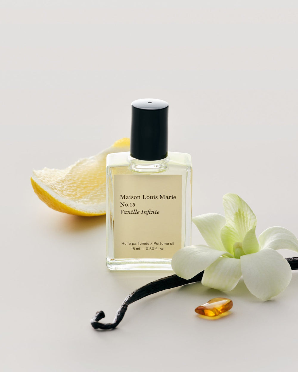 Perfume bottle labeled 'Maison Louis Marie' with vanilla pod, orchid, and lemon on a light background