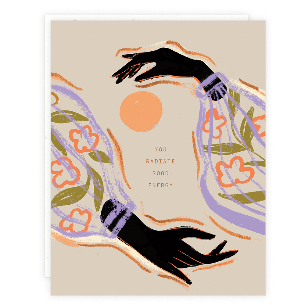 Two dark-skinned hands with illustrated floral sleeves reach toward each other in a circle on the Good Energy print, surrounded by a peach sun and the text You radiate good energy with foil details.