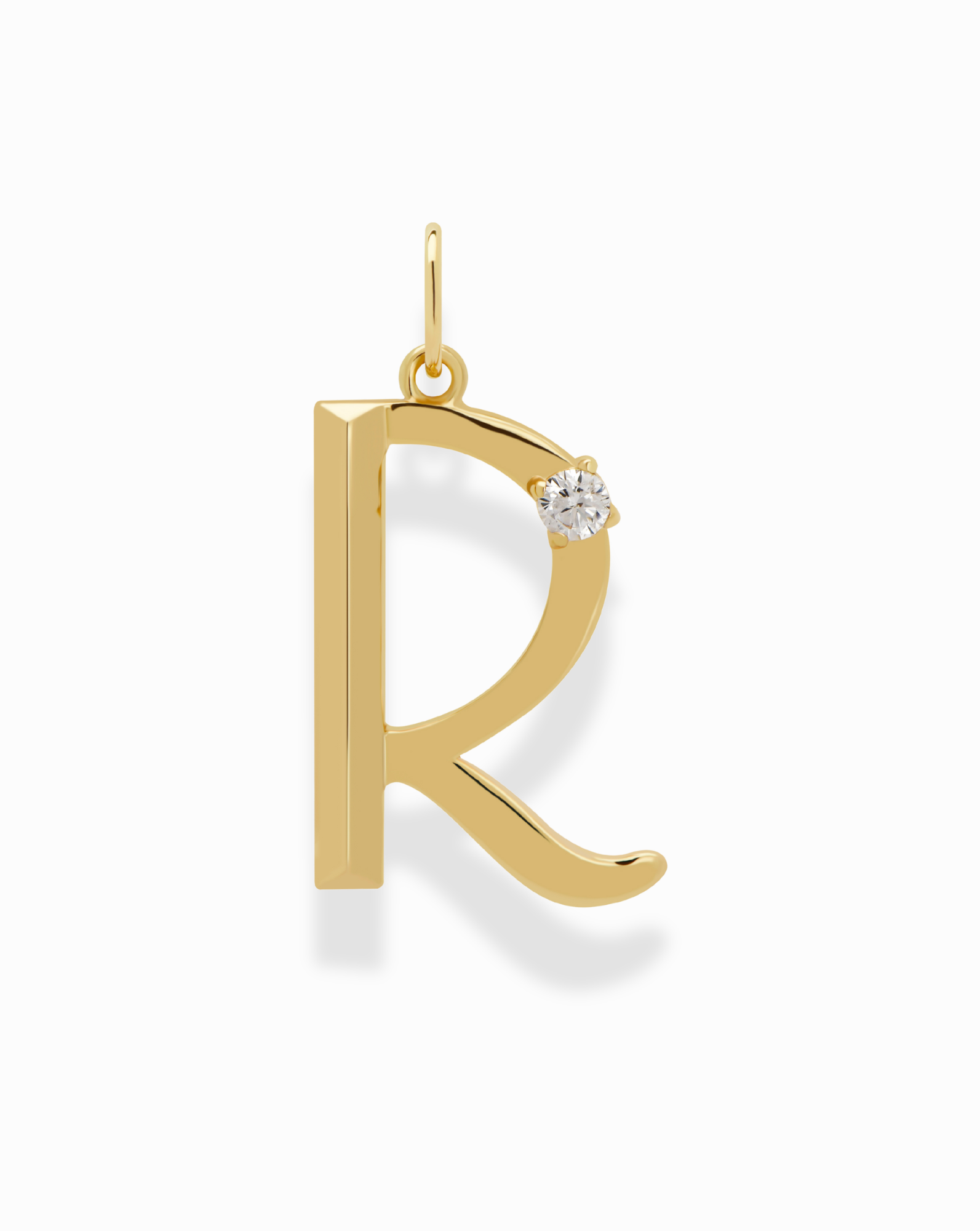 The Eloise Letter Charm by Mod + Jo features a gold R-shaped design with a small white gemstone near the top right, a polished finish, and a loop for adding to your personalized necklace.