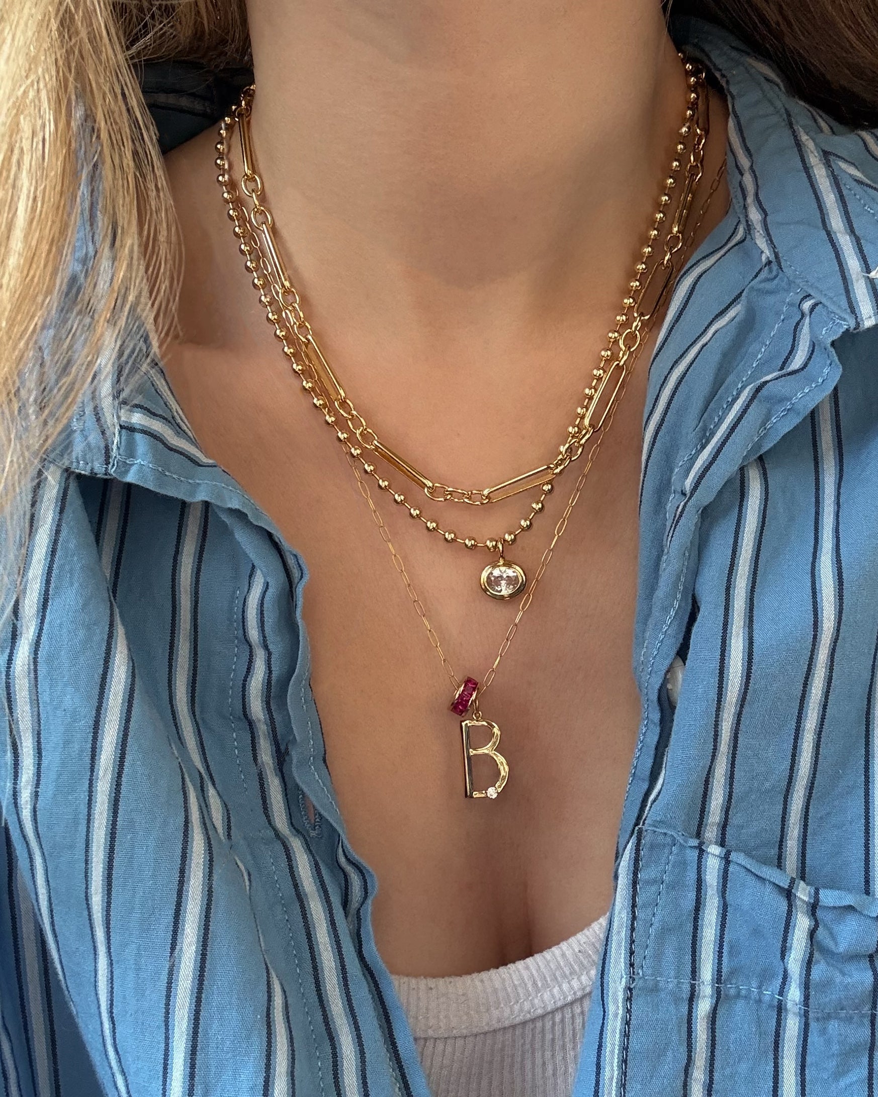 A person wearing Mod + Jo's Soren Ball Chain Necklace layered over a white top and blue striped button-up shirt.