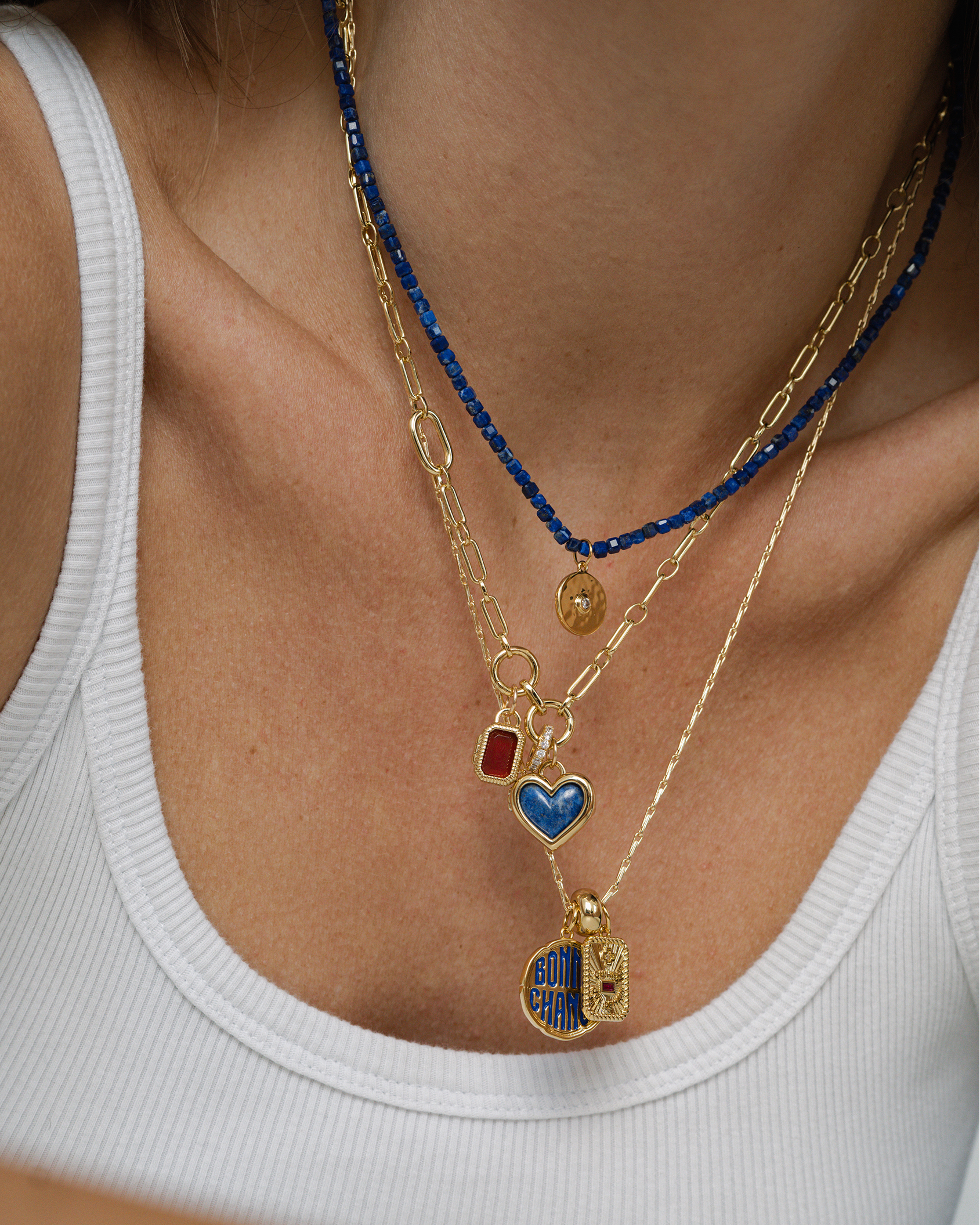 Close-up of a person wearing multiple gold necklaces with various pendants.