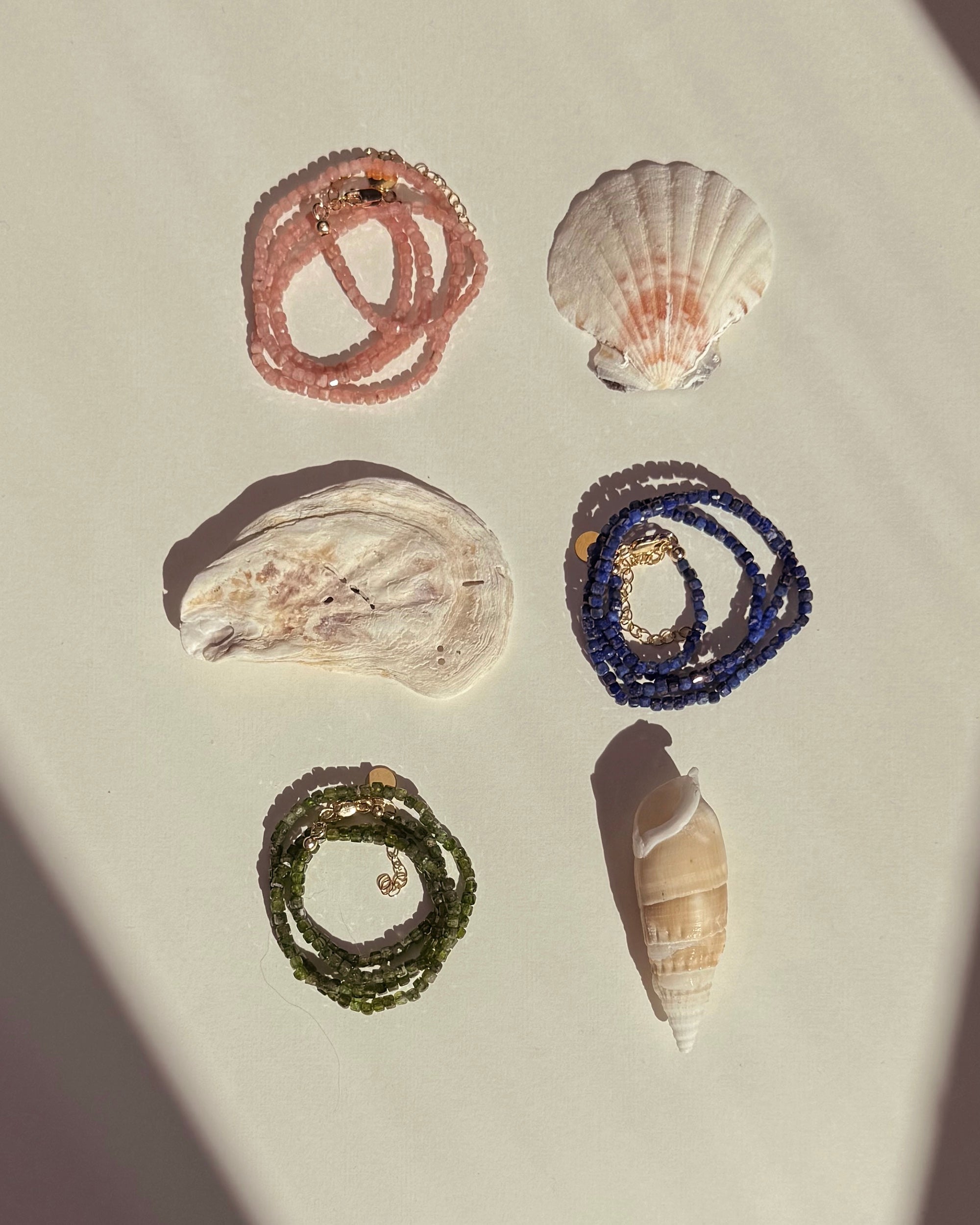 The Mod + Jo Merit Gemstone Necklace is displayed on a bright surface in natural sunlight, paired with three seashells for a coastal vibe. Perfect for layering with your favorite 14k gold-filled jewelry.