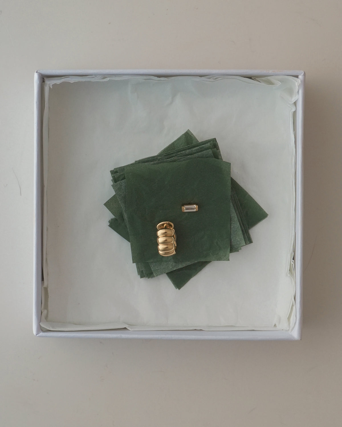 Sylvie + Jadey Set consisting of gold hoop earrings and baguette studs resting on a stack of green tissue paper inside a white gift box.