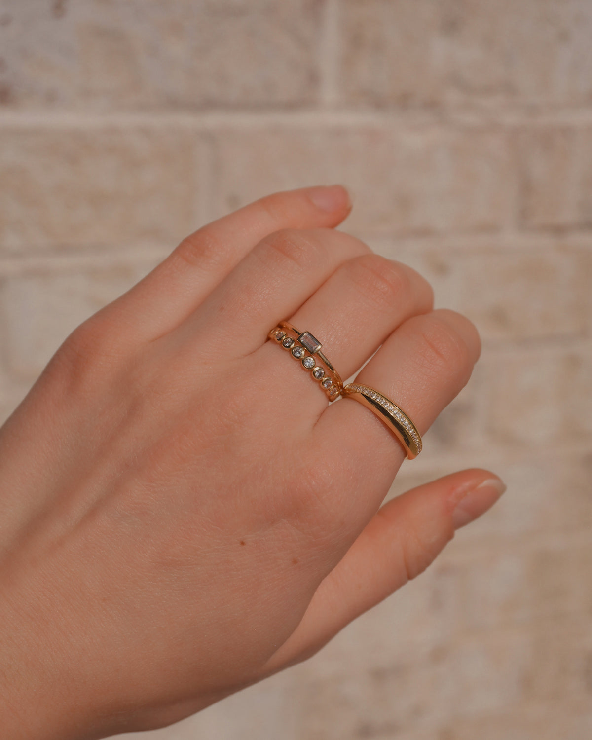 A hand wearing the Nina + Blair + Evelyn Set by Mod + Jo, featuring a horizontal baguette ring, a row of circular stones, and an eternity band with a channel of small stones.