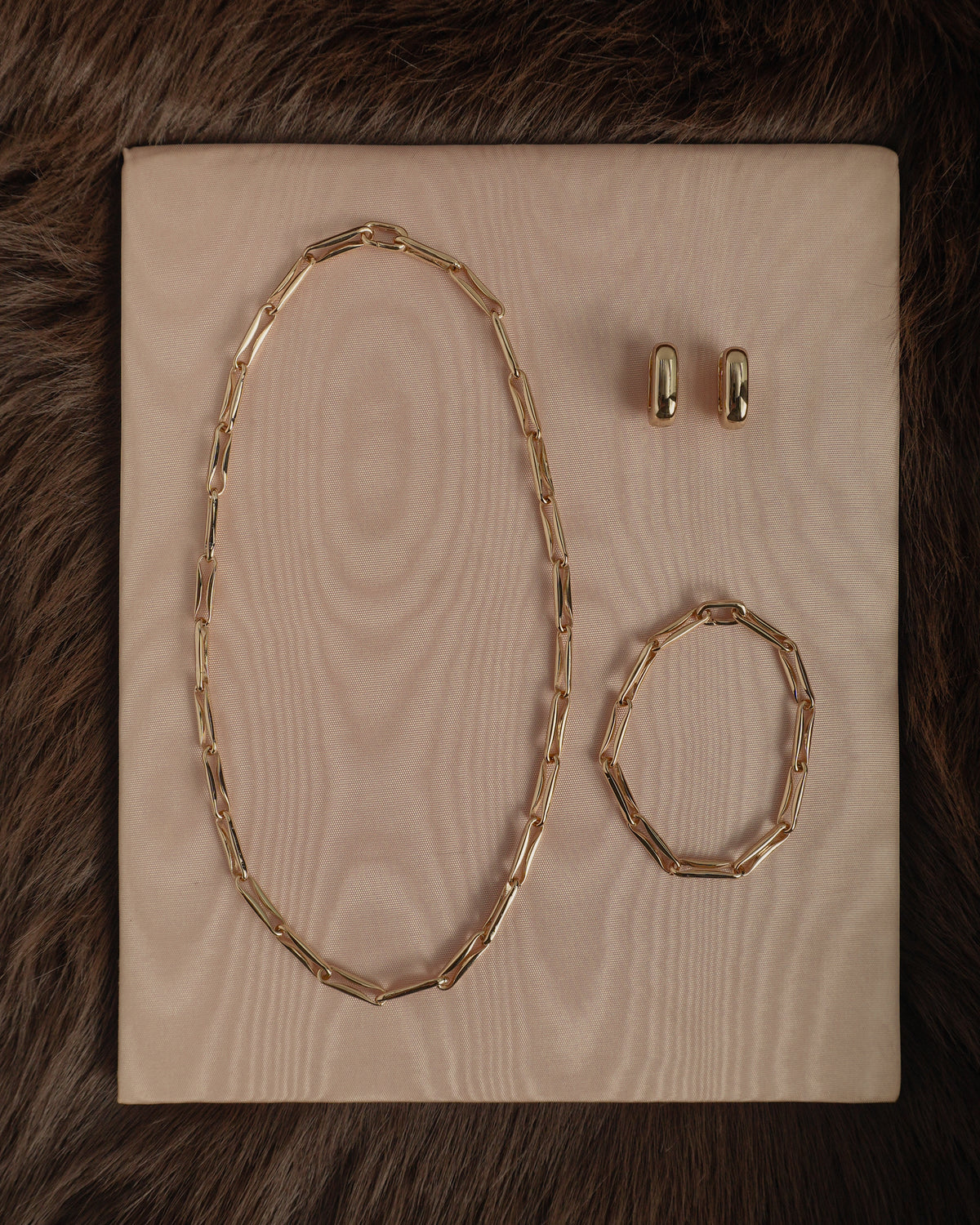 The Barely-There Trio Set by Mod + Jo, a gold-toned jewelry set featuring an elongated link chain necklace, a matching elongated link chain bracelet, and a pair of petite hoops.