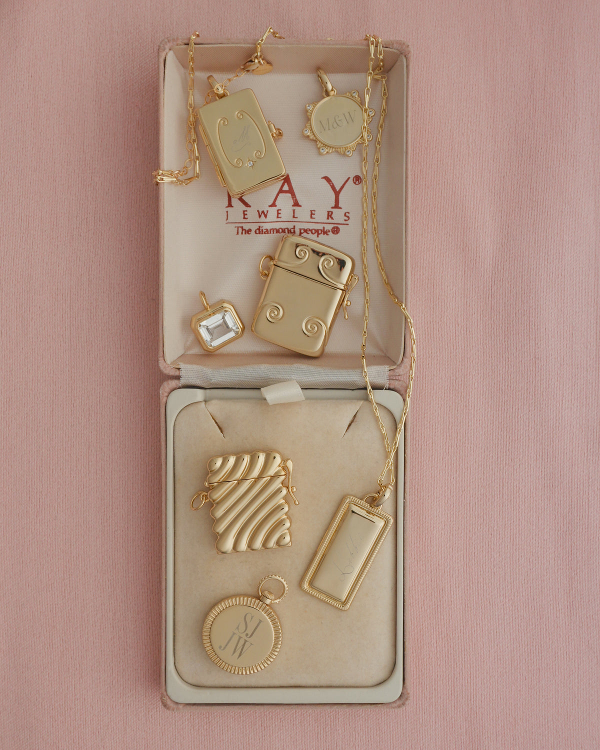 A selection of gold-tone Remi Engravable Charm pendants and cubic zirconia charms displayed in an open jewelry box.