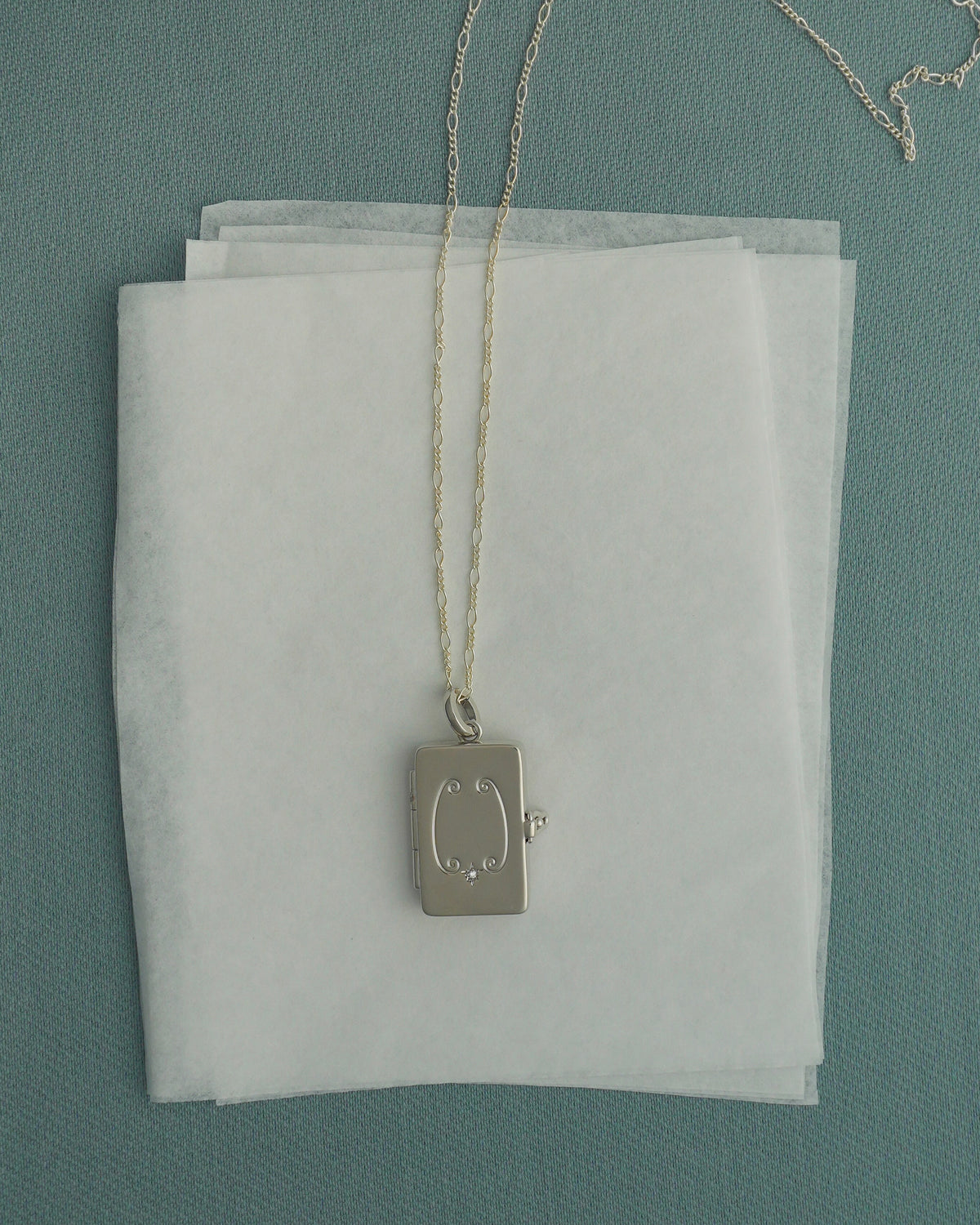 A rectangular silver Delphine Locket Charm with a small star-set stone on a delicate chain.