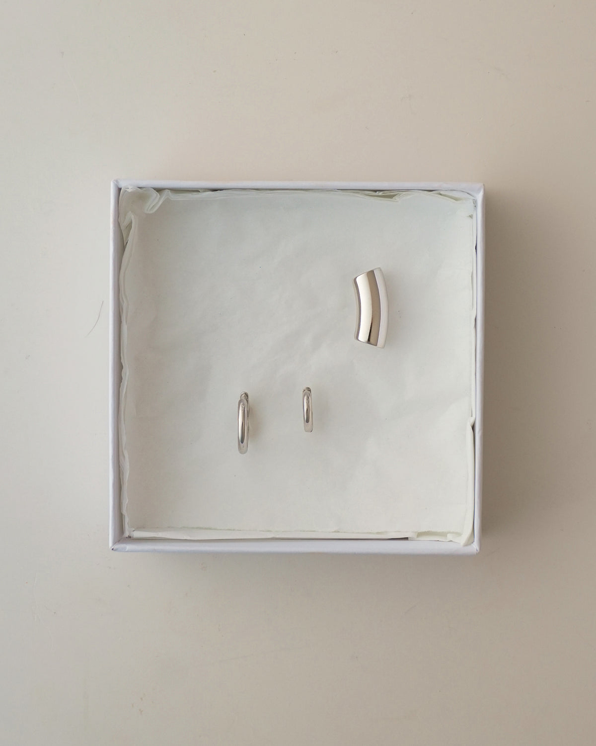 A Reneé + Lennon Set featuring two silver smooth huggies and a single curved silver ear cuff inside a white gift box.