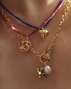 Necklace with various charms including a number '13' and a hand holding a pearl, worn on a person's neck.