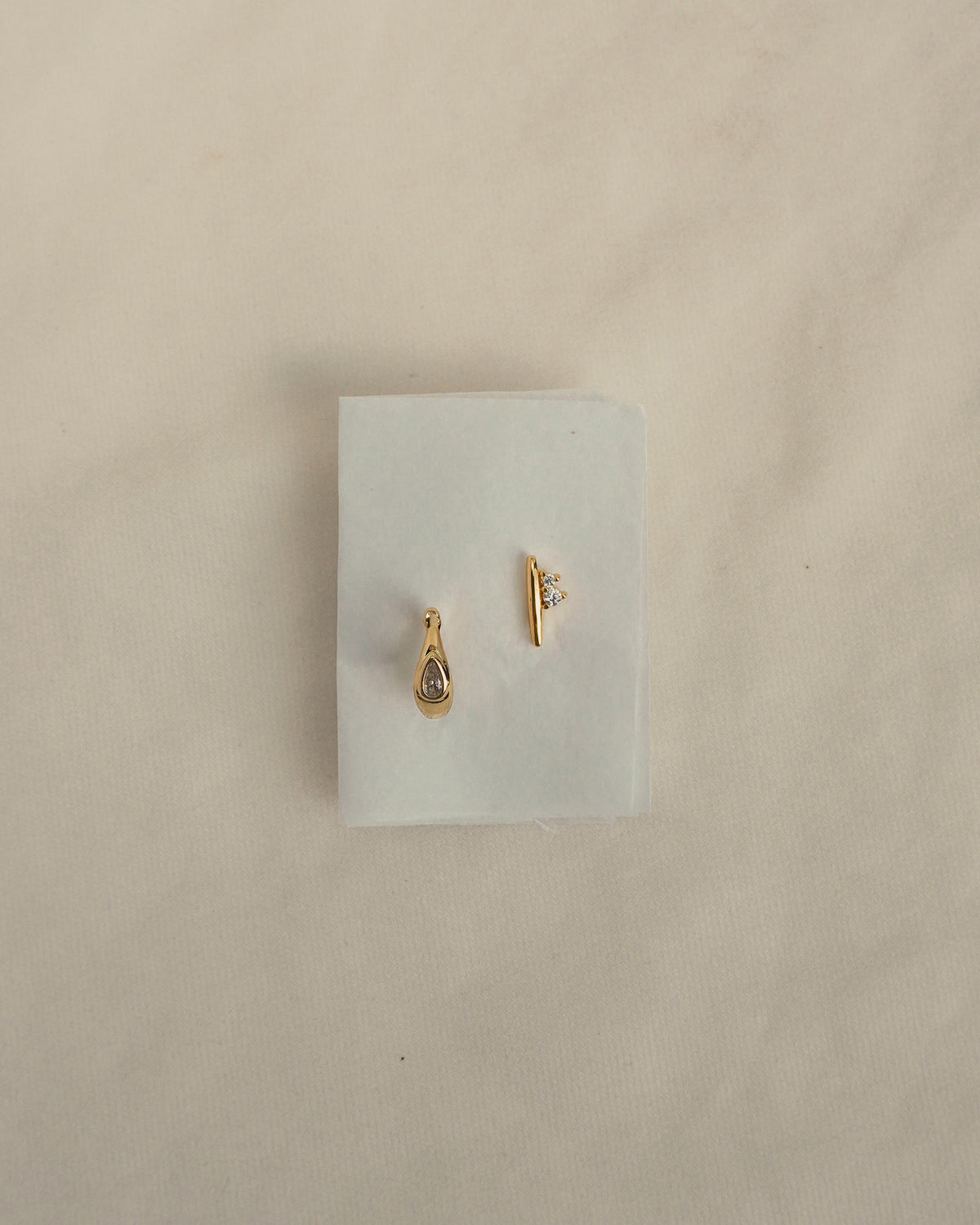 Mod + Jo Ida + Tally Set consisting of a gold-tone pear huggie hoop earring with a small crystal and a gold-tone bar stud earring with two small crystals.