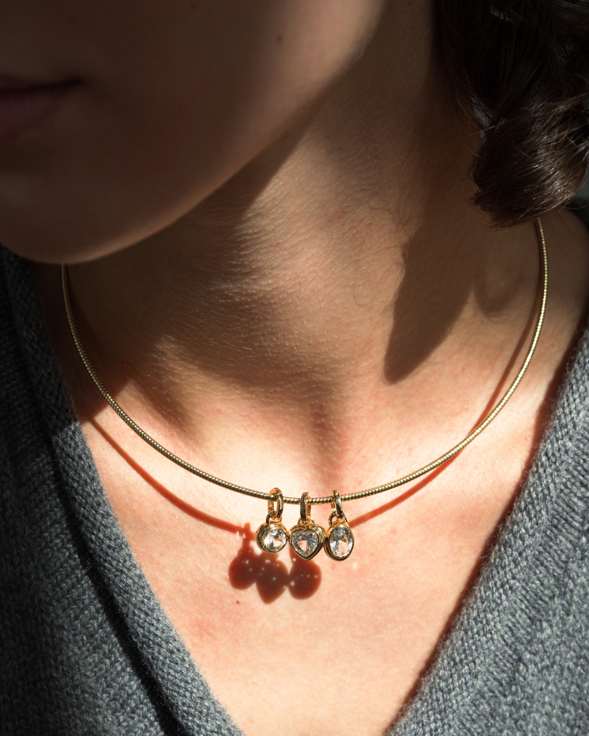 Celine Collar Necklace by Mod + Jo, a gold rigid collar featuring three small sapphire charms: two round gems flanking a central heart-shaped gem.