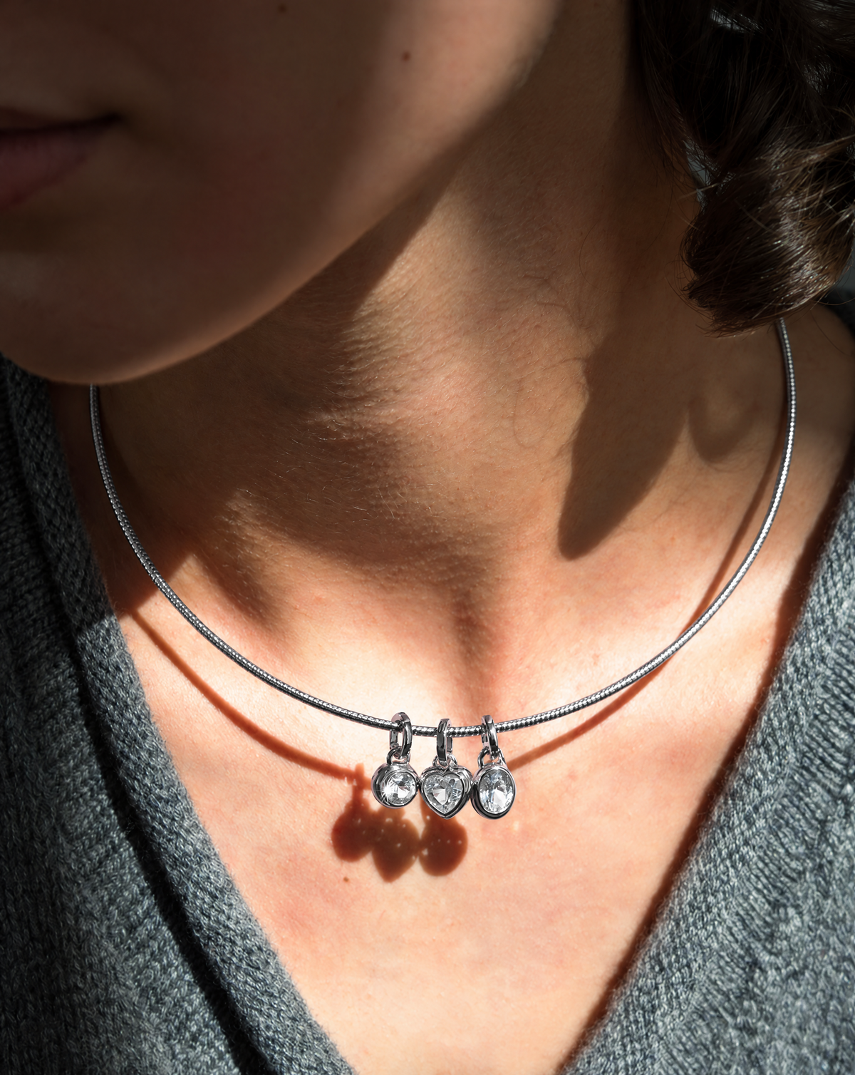 Celine Collar Necklace by Mod + Jo, a silver rigid collar featuring three small dangling charms with clear stones, including one heart-shaped charm.