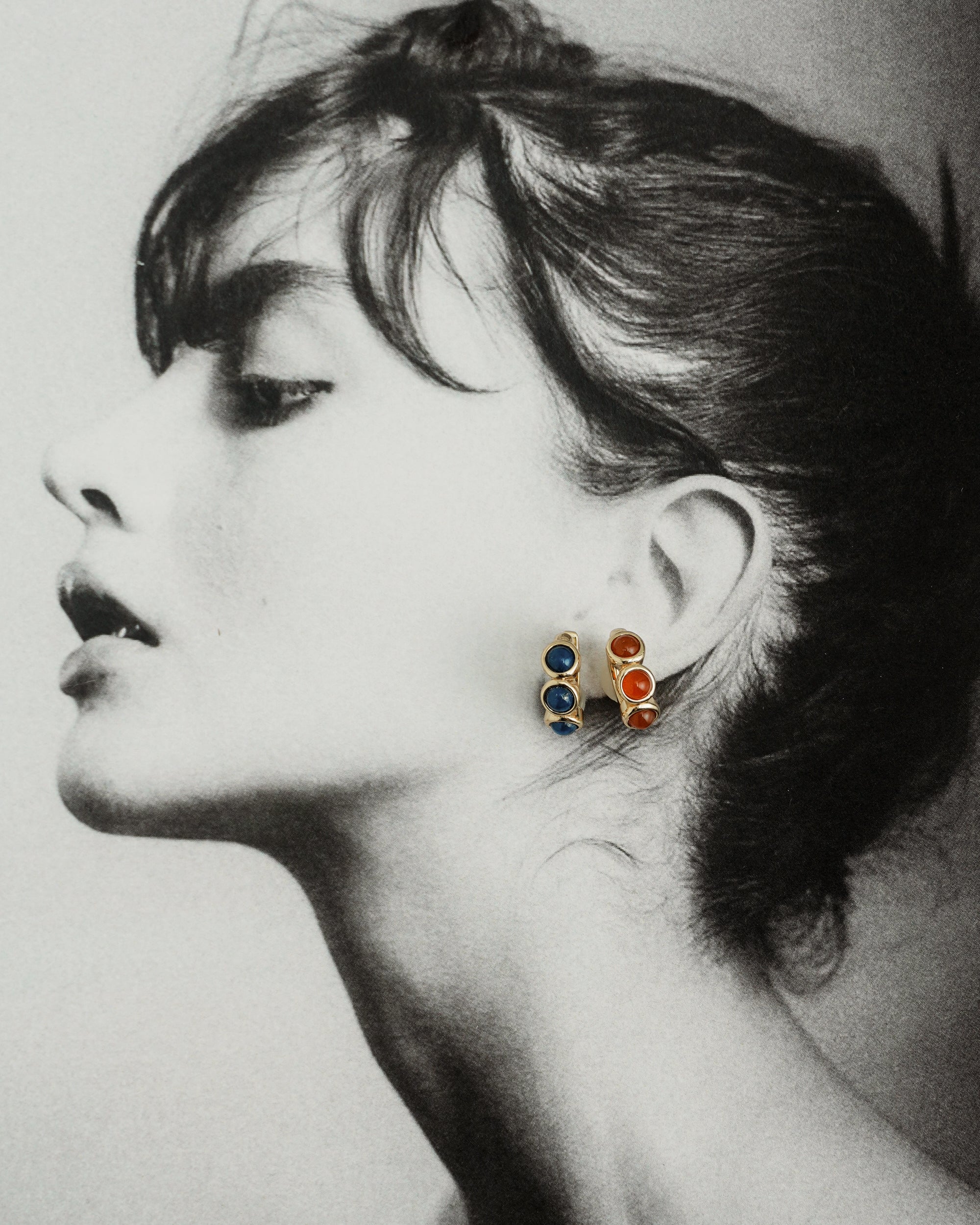 Black and white profile of a woman with dark hair in an updo, wearing Mod + Jo *Preorder* Corynn Gemstone Huggies featuring natural lapis lazuli and 18k gold plated accents, gazing upward with a serene expression.