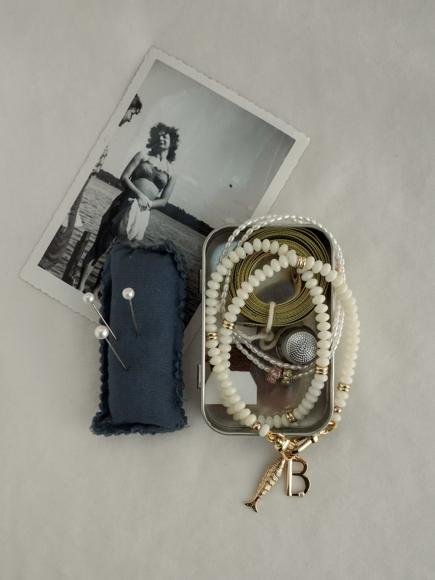 A red velvet jewelry box holds gold hoop earrings and a personalized Mod + Jo Eloise Letter Charm necklace with an S initial and star pendant. Another gold letter charm necklace and glass bottles rest on a white surface.