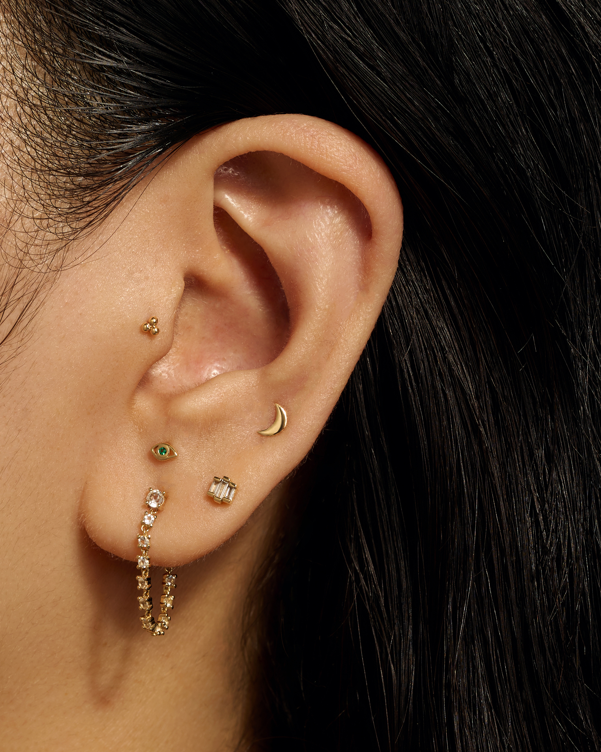 Close-up of an ear with multiple gold earrings against a dark background