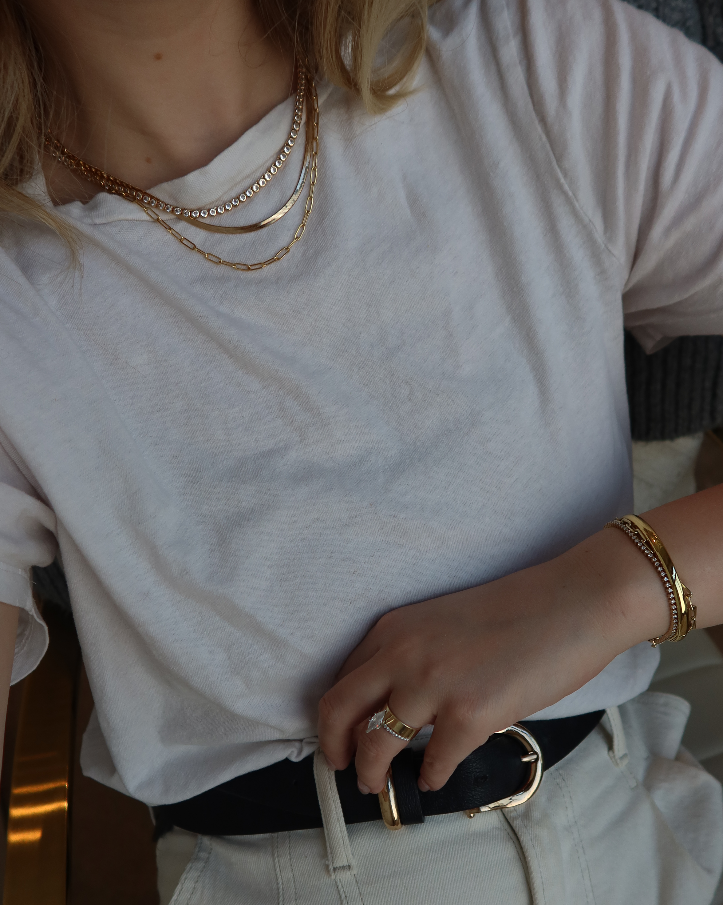 Person wearing a white t-shirt, black belt, and gold jewelry.