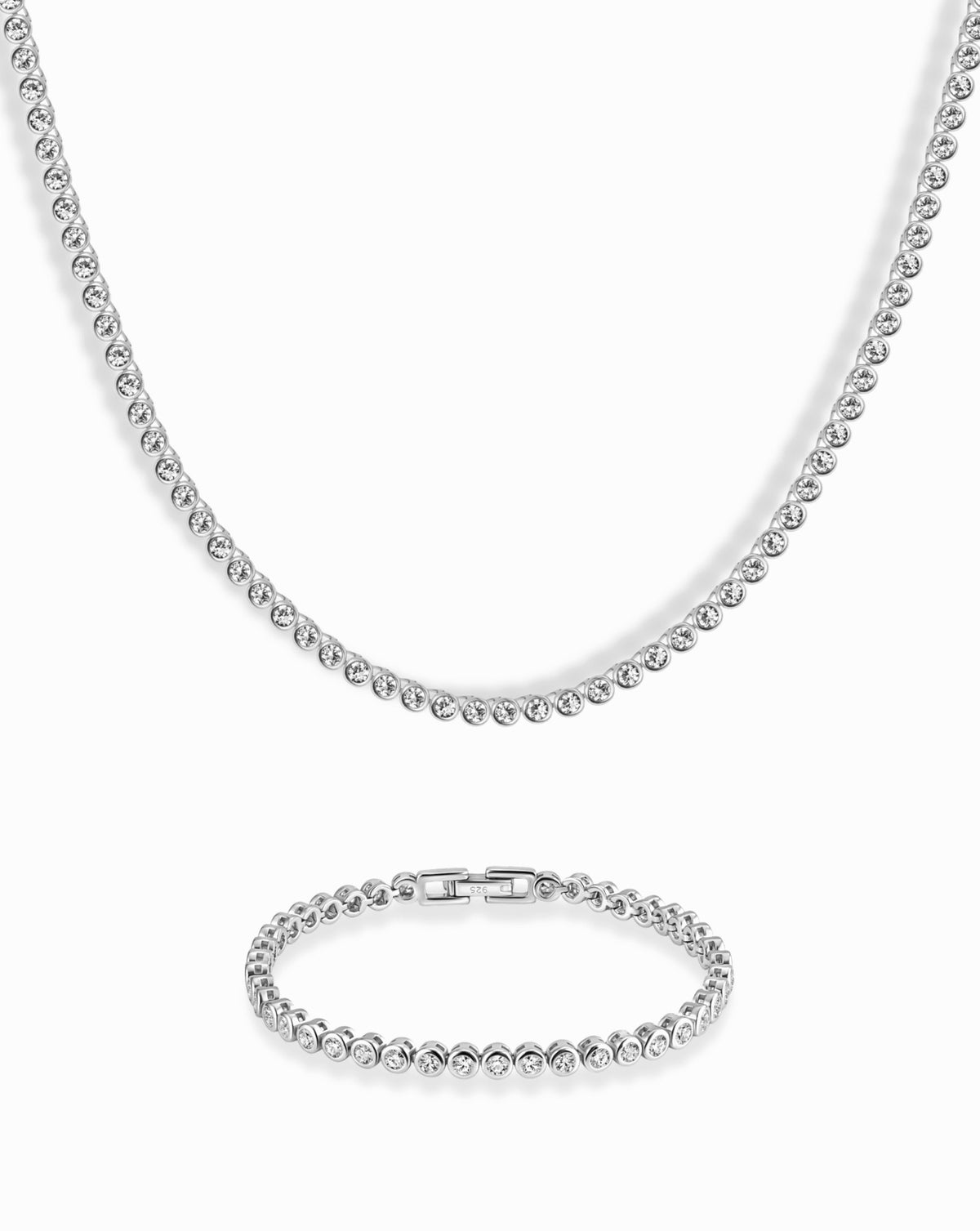 The Emma Set features a silver-tone bezel tennis necklace and bracelet set with a continuous row of round, bezel-set clear stones.