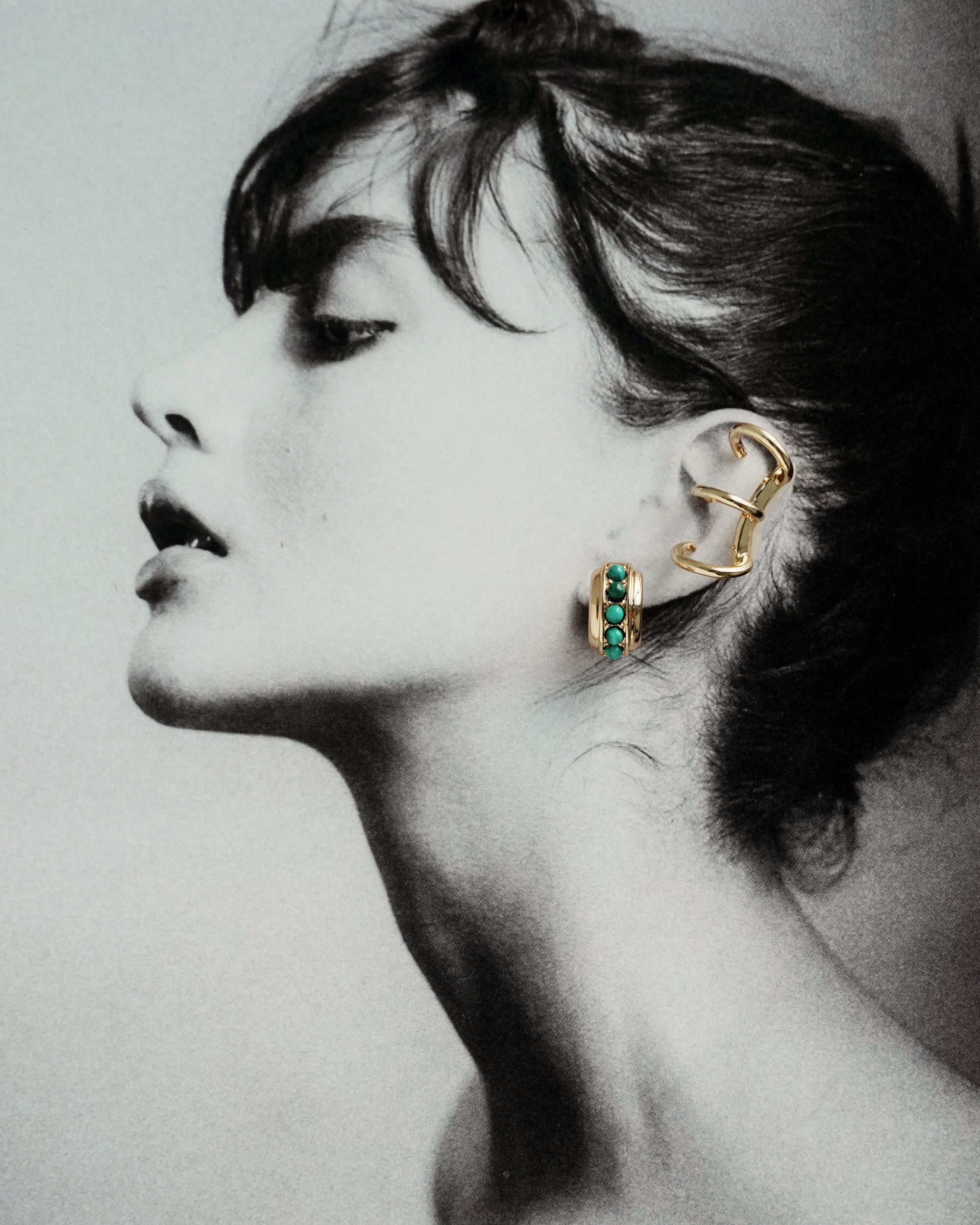 Black and white profile of a woman with dark hair, lips parted, wearing Mod + Jo’s *Preorder* Eli Tripple Helix Ear Cuff in 18k gold on her upper ear and a turquoise stone no-piercing cuff on her lower ear.
