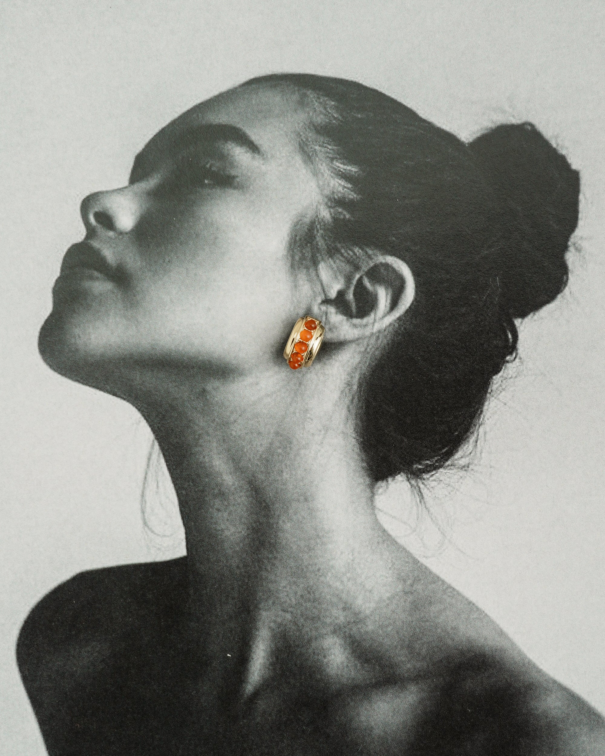 Black and white side profile of a woman with her hair in a bun, wearing Mod + Jo’s *Preorder* Evy Raised Gemstone Hoops with red accents. Her chin is slightly lifted, highlighting her neck and jawline.