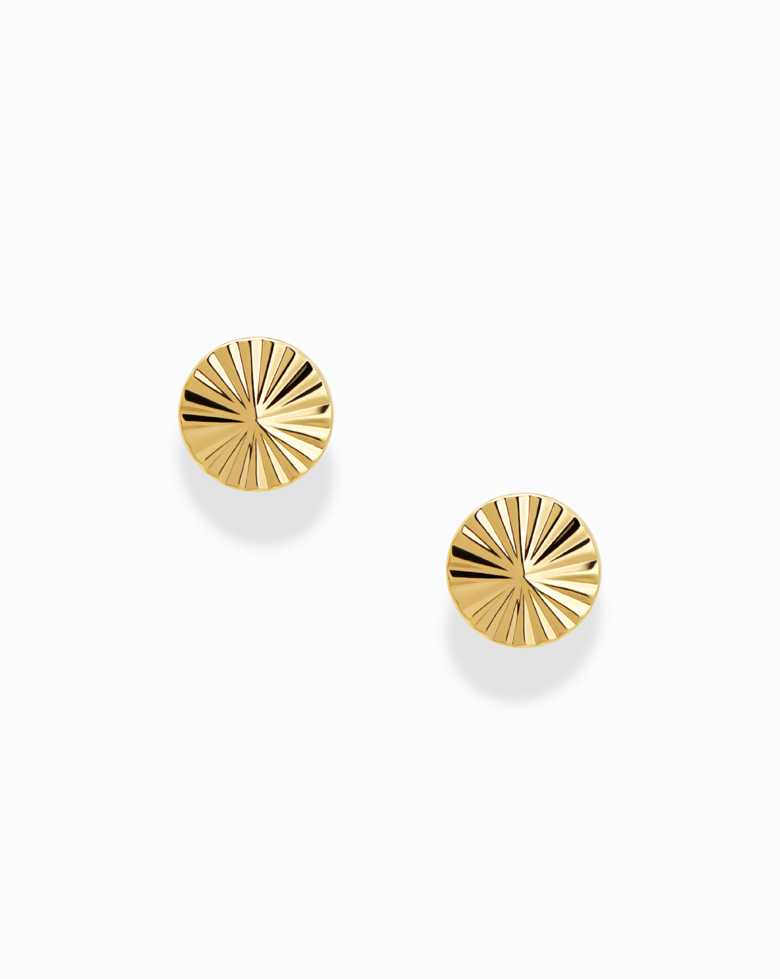 The Mod + Jo Dela Fluted Studs are a pair of round, gold-tone stud earrings featuring a sunburst engraved pattern reminiscent of classic fluted designs, displayed on a white background.