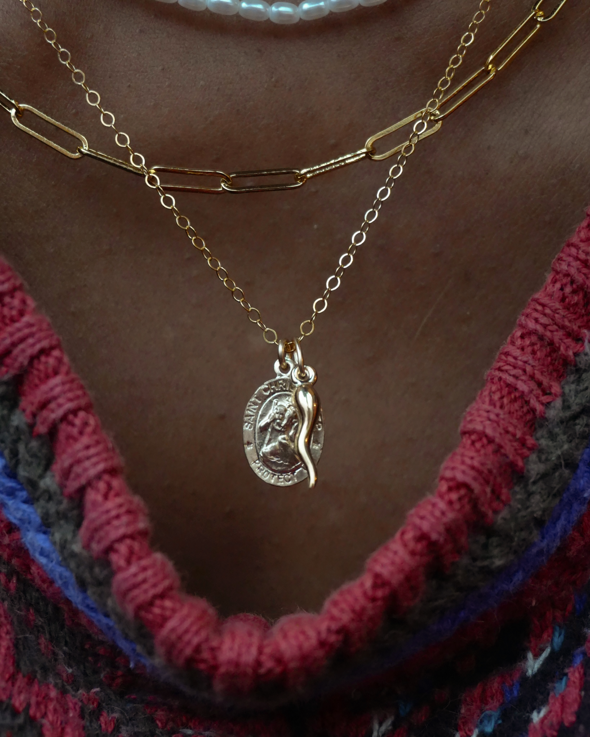 Gold necklace with a pendant on a person wearing a colorful garment.