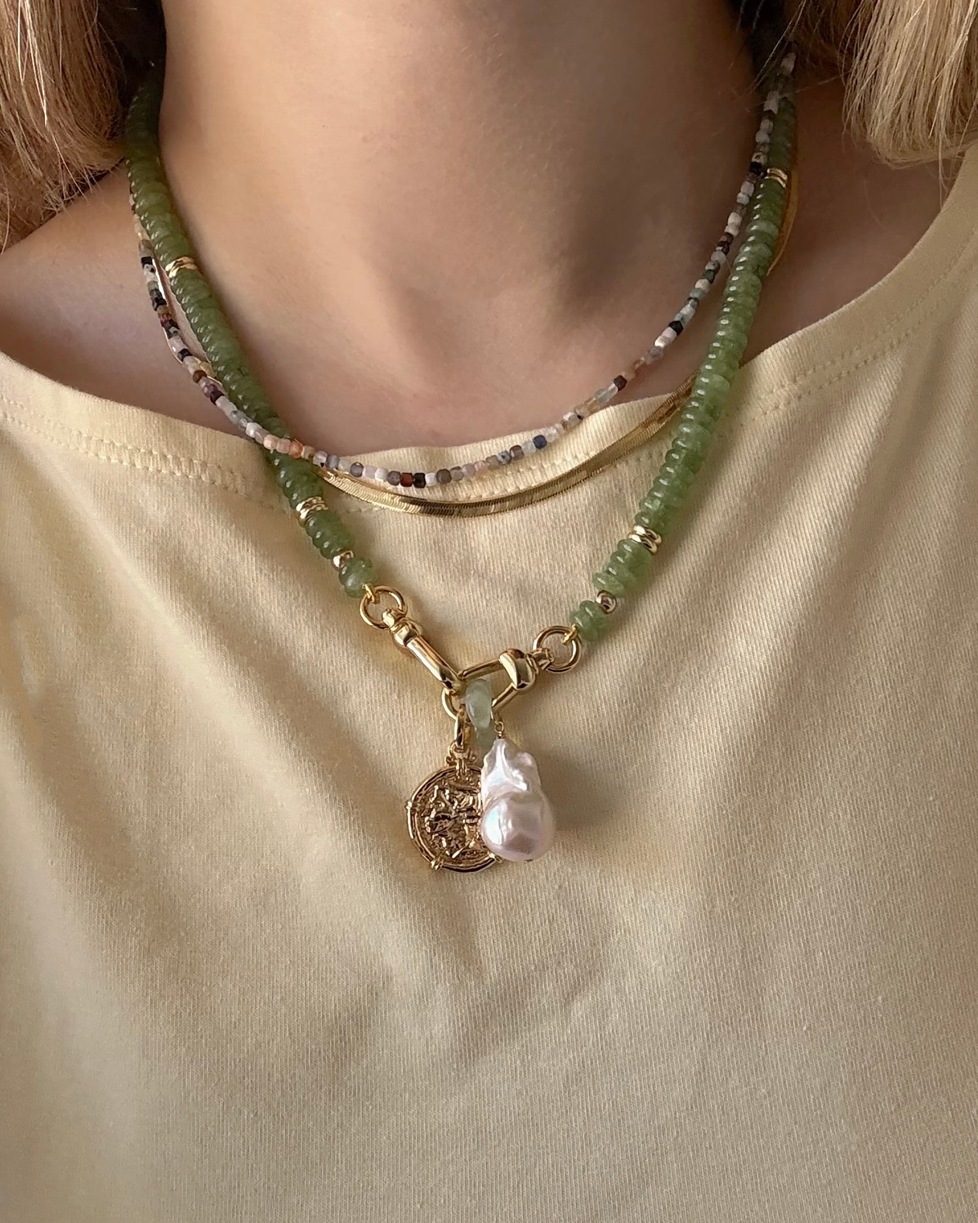 Close-up of a person wearing the Mod + Jo Merit Gemstone Necklace with multicolored beads, layered with a 14k gold-filled pearl and coin pendant, styled over a light yellow tee. All pieces are handmade in Dallas.