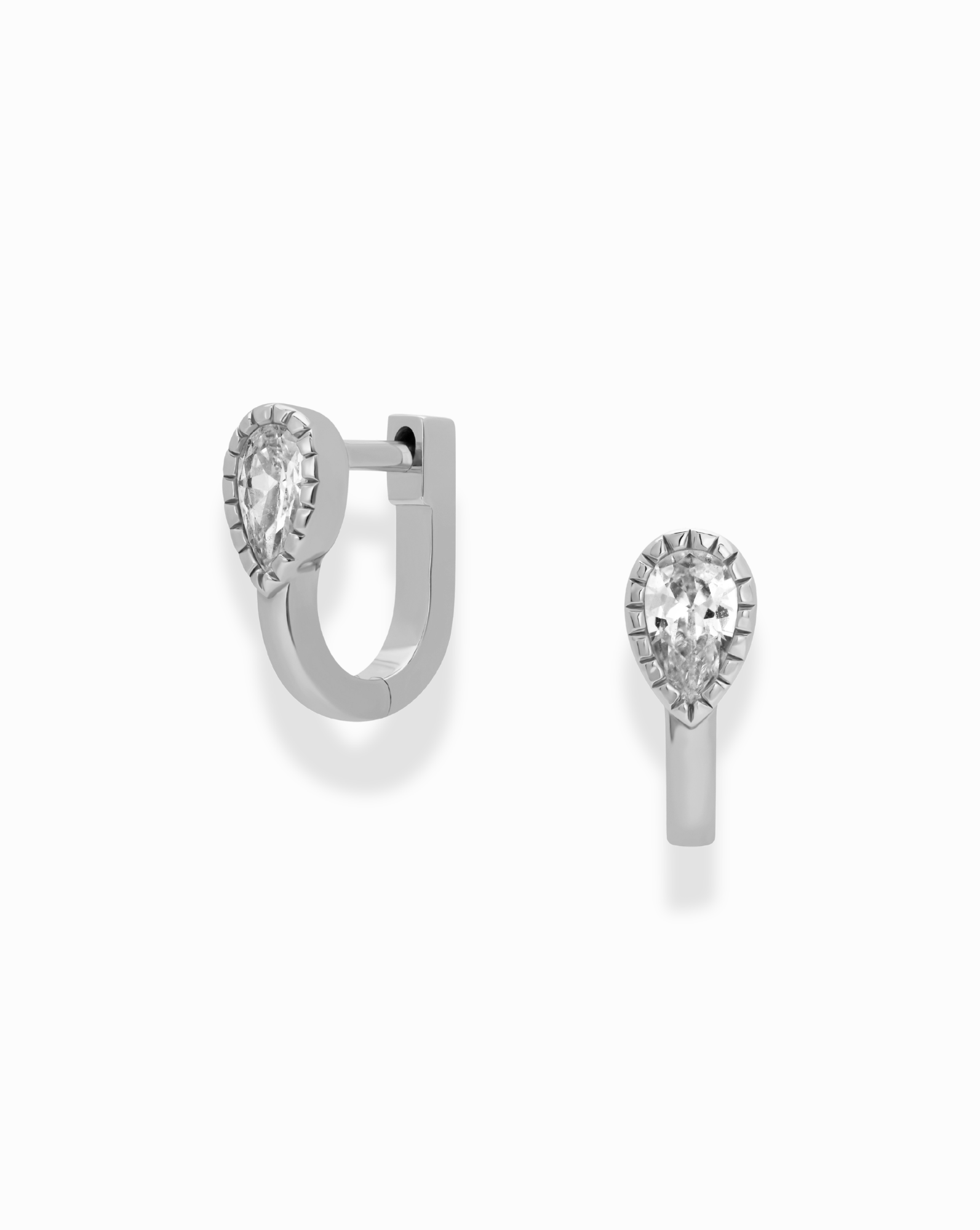 Mod + Jo’s Leighton Teardrop Huggies, a pair of rhodium plated earrings featuring pear-shaped clear cubic zirconia gemstones, are shown on a white background—one displayed from the front and the other highlighting its clasped side view.