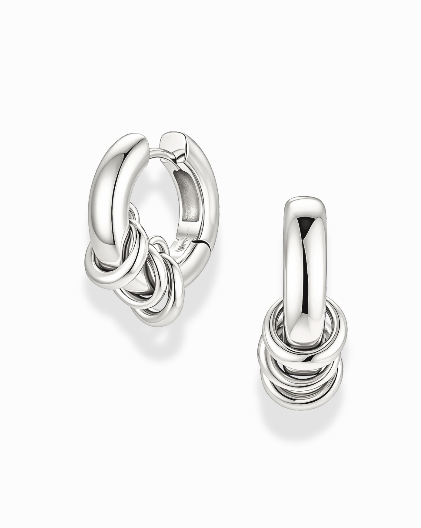 The Mod + Jo Grande Levi Huggies are a pair of shiny silver, rhodium plated statement earrings, each featuring three small interlocking rings at the bottom. Displayed on a plain white background, these modern huggie earrings add a touch of elegance to any look.