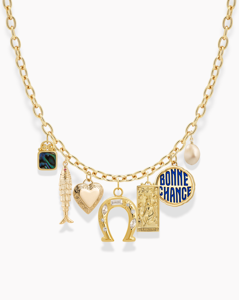 A gold chain necklace with seven charms: a square black and green charm, a gold fish, a gold heart, a jeweled horseshoe, a rectangular gold tag, a blue BONNE CHANCE oval charm, and a white pearl.