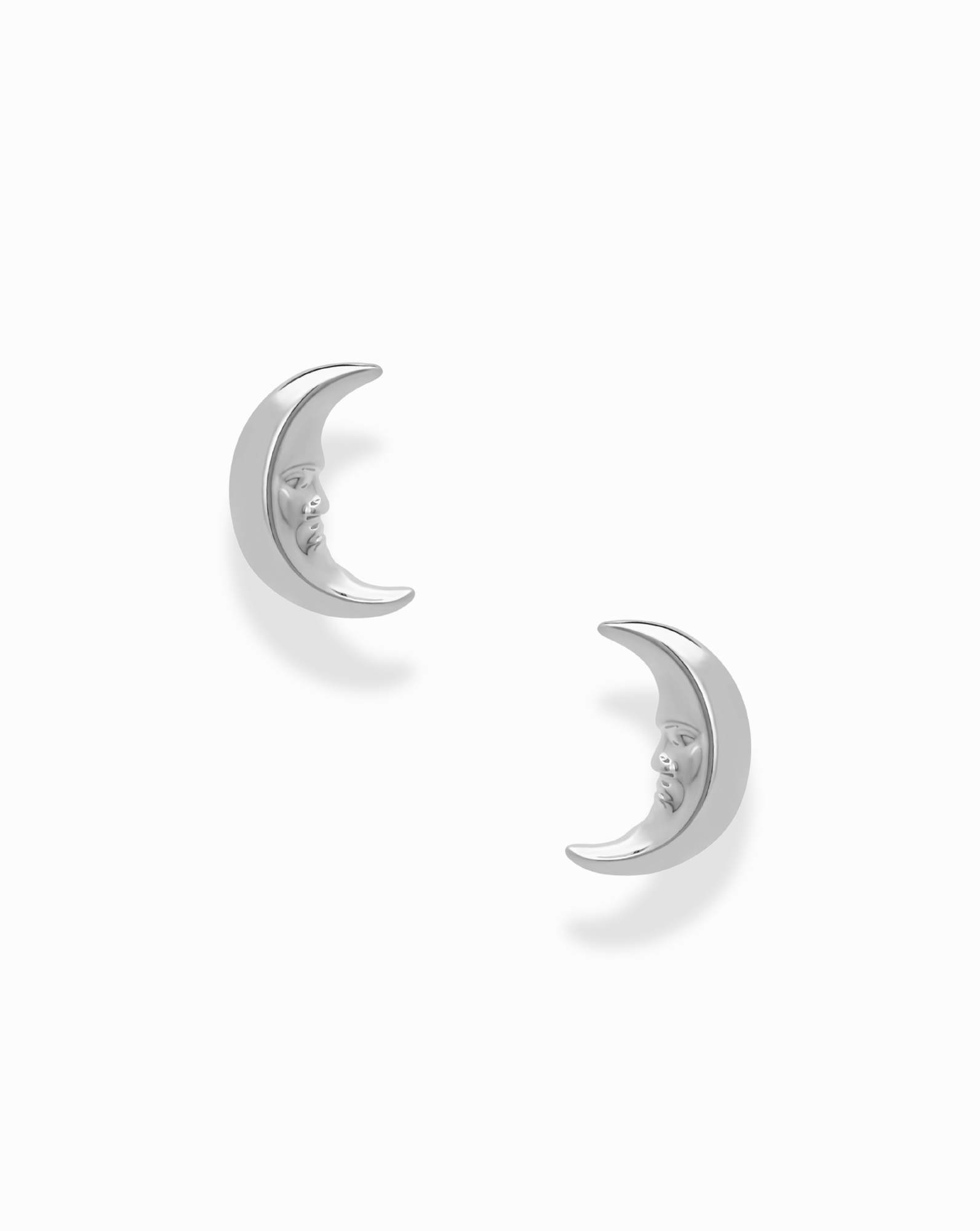 A pair of Archie Moon Studs by Mod + Jo—silver crescent moon earrings featuring engraved facial details—are displayed on a plain white background. These celestial studs are rhodium-plated for enhanced shine and durability.