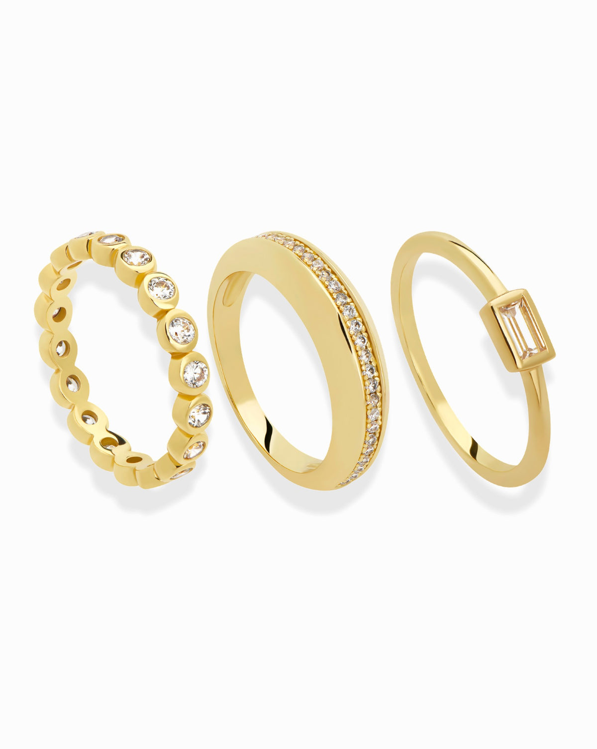 The Mod + Jo Nina + Blair + Evelyn Set features three gold rings: an eternity band with a full circle of bezel-set round stones, a stacking ring with a pavé center, and one featuring a single baguette stone.