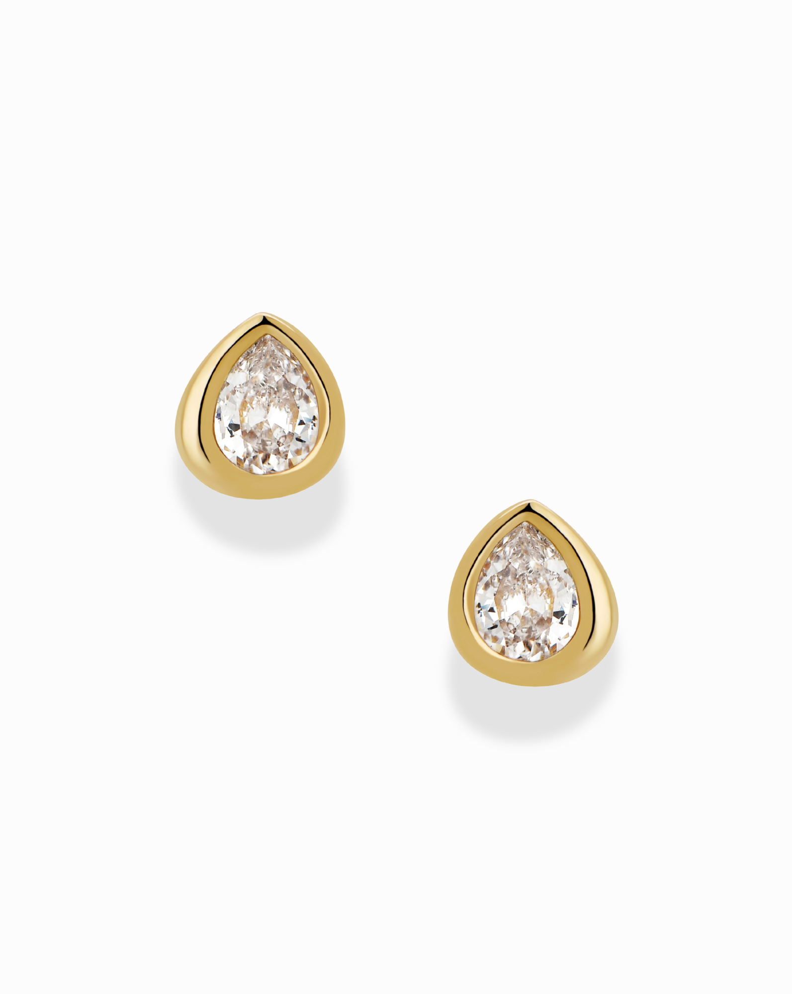 The Joni Bezel Studs by Mod + Jo are gold-plated earrings, each showcasing a clear, pear-shaped cubic zirconia gemstone in a simple bezel setting and displayed on a white background.