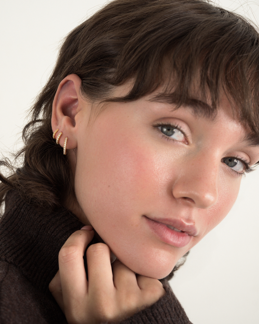 Close-up of a person wearing two small, gold Reese Gift Set hoops encrusted with clear pavé stones in their earlobe.