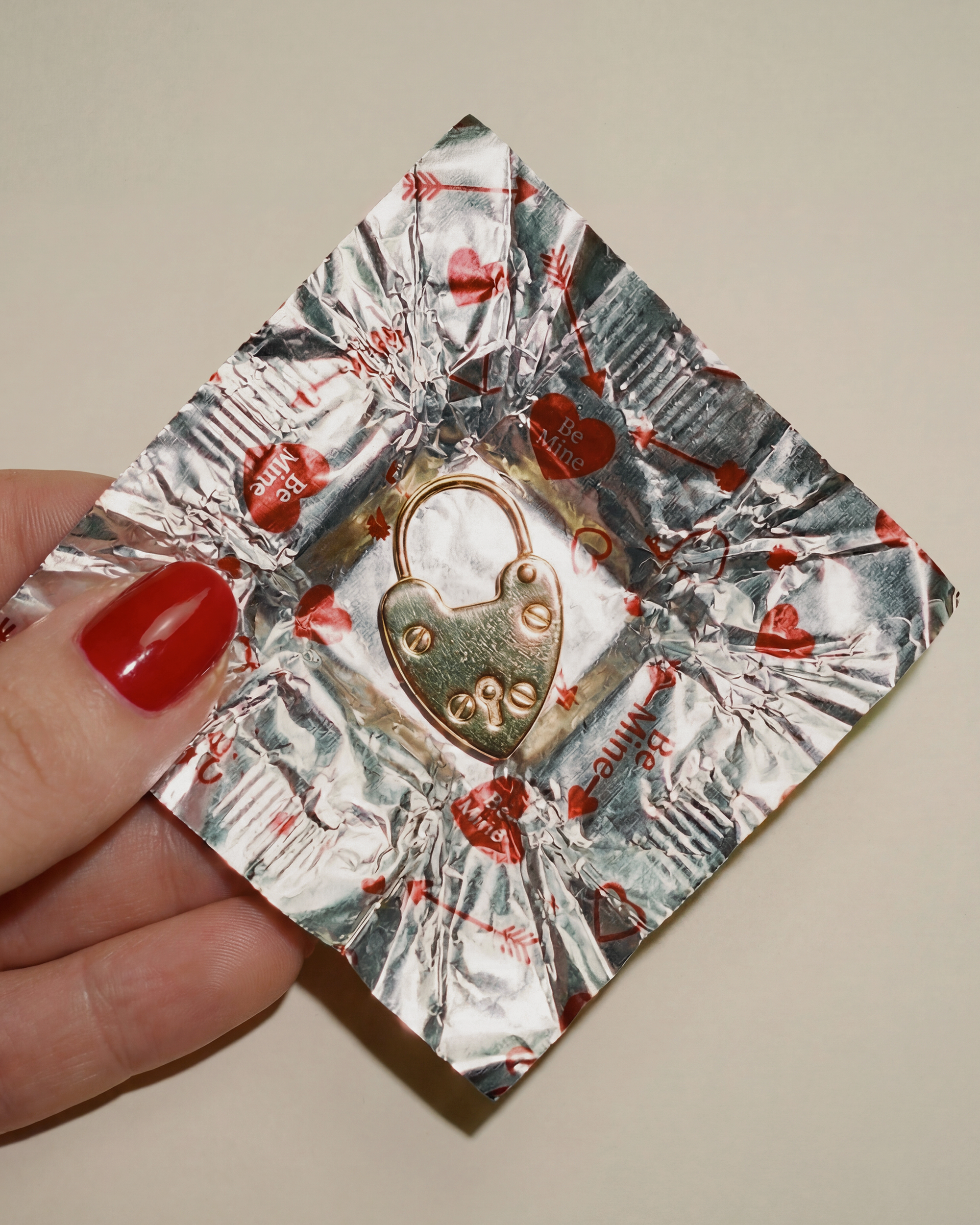 Hand holding a chocolate foil square with heart lock charm inside.
