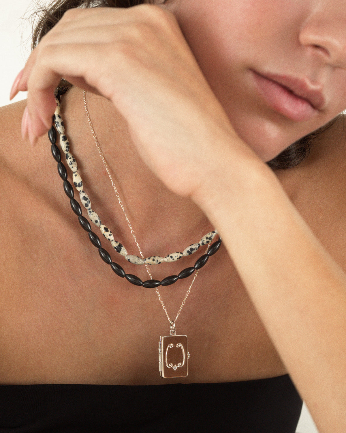The Sutton Gemstone Necklace features three layered strands: black agate beads, spotted rice-shaped stones, and a delicate 18-inch chain with a rectangular locket pendant.