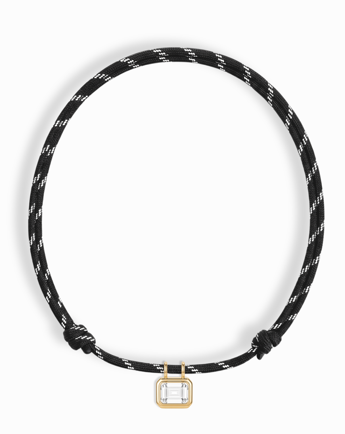 Introducing the Mod + Jo Tommy Sapphire Pendant Necklace—an adjustable black and white paracord necklace accented with a small, rectangular gold bezel-set pendant that showcases a clear, lab-grown white sapphire at its bottom center.