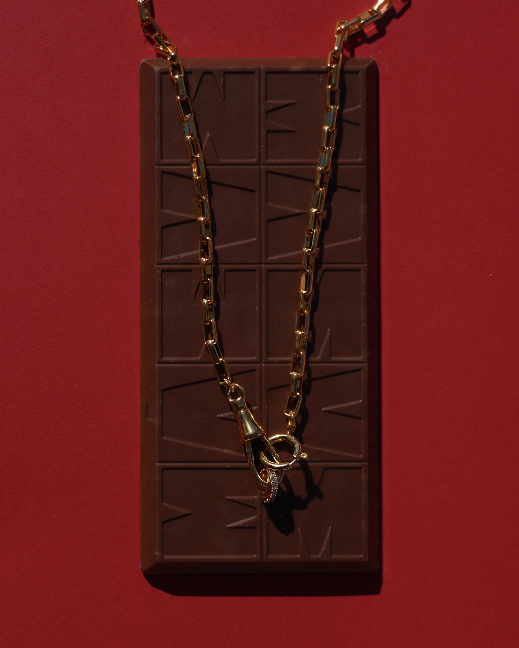 Gold chain necklace on a chocolate bar against a red background