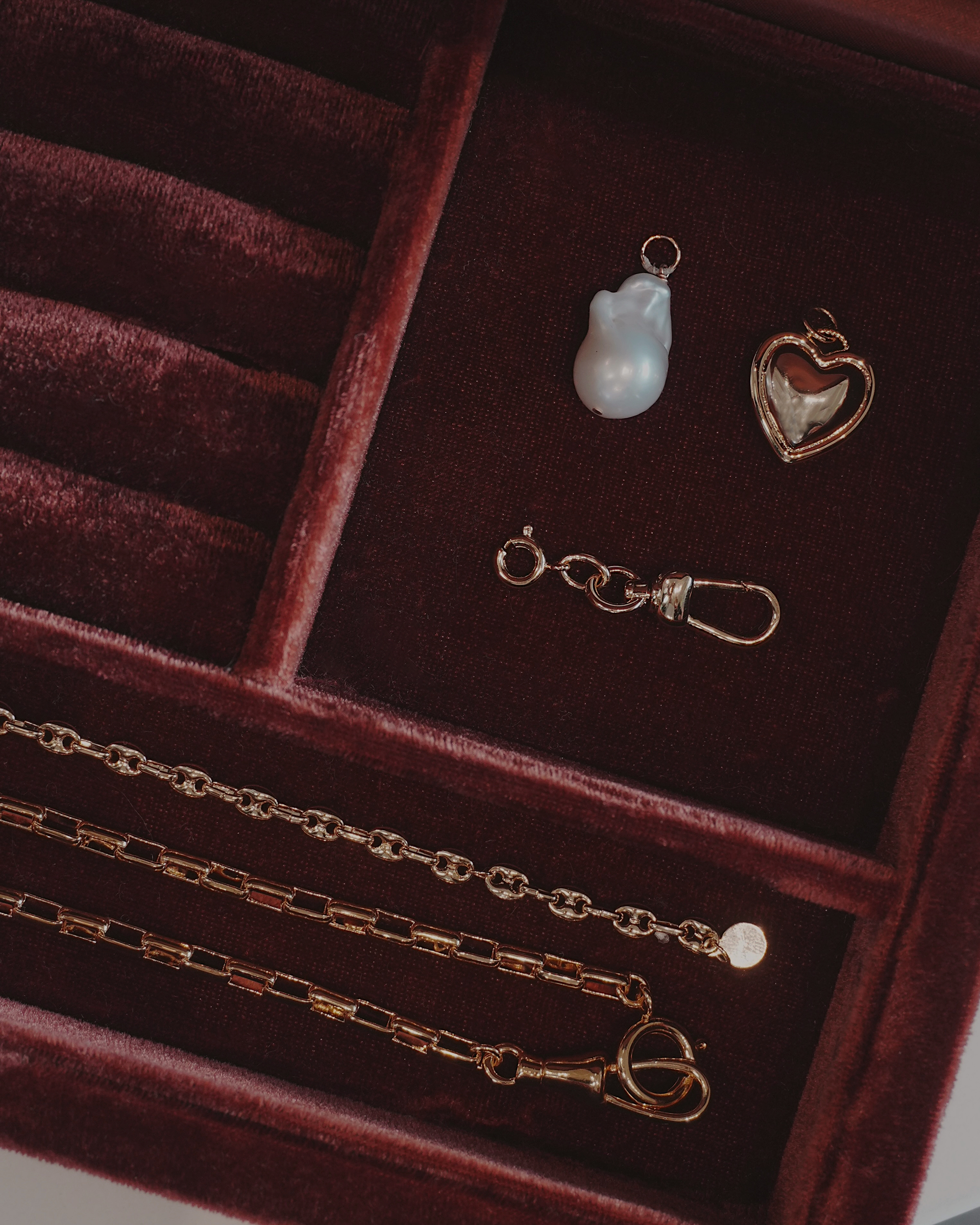 Jewelry set including a gold chain, pendant, and earring on a dark red velvet surface.